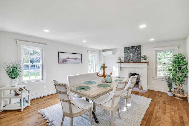 dining space with a brick fireplace, light wood-type flooring, a wall unit AC, and a healthy amount of sunlight