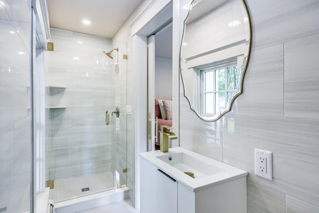 bathroom with a shower with door, vanity, and tile walls