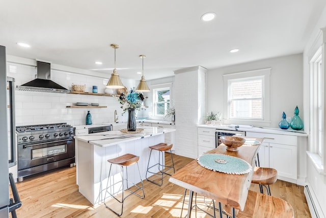 kitchen with white cabinets, wall chimney exhaust hood, decorative light fixtures, a baseboard heating unit, and high end appliances