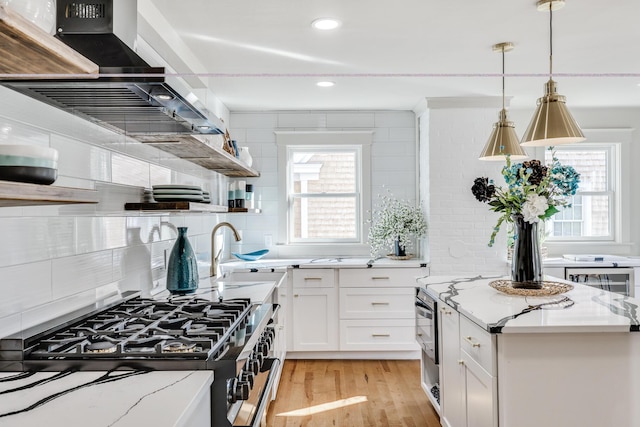 kitchen with stainless steel range with gas stovetop, white cabinetry, light stone counters, and island range hood