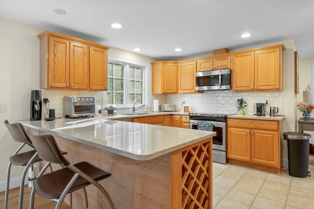 kitchen featuring light tile patterned floors, stainless steel appliances, backsplash, a sink, and a peninsula