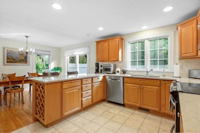 kitchen with a peninsula, stainless steel appliances, light countertops, pendant lighting, and a sink