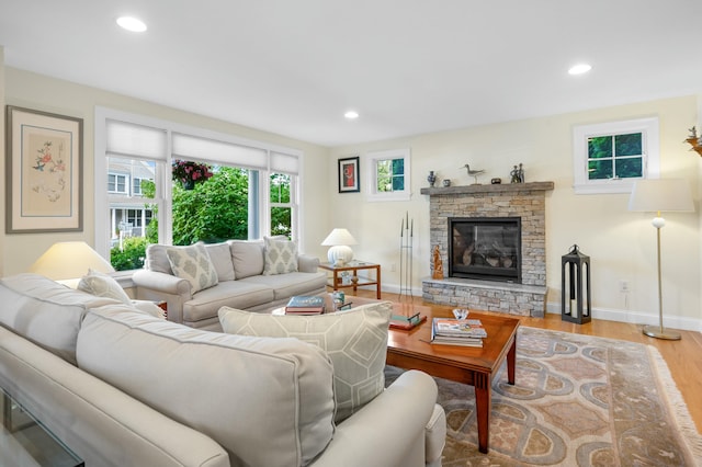 living room with baseboards, a stone fireplace, light wood finished floors, and recessed lighting