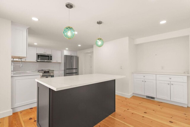 2 Little Cove Ln, Orleans, MA 02653 - kitchen with stainless steel appliances, white cabinets, light wood-style floors, backsplash, and decorative light fixtures