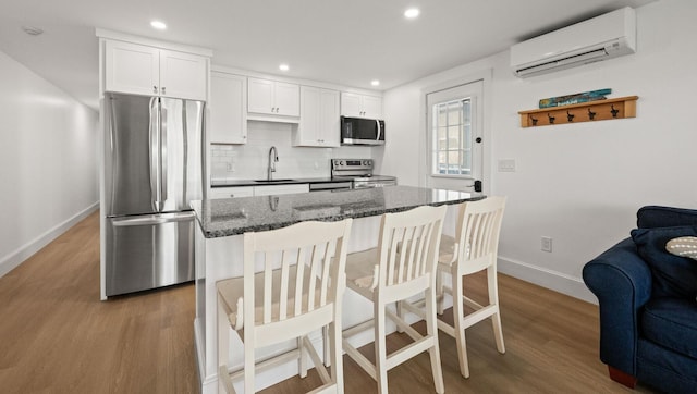 kitchen featuring a wall unit AC, appliances with stainless steel finishes, white cabinetry, tasteful backsplash, and dark stone countertops