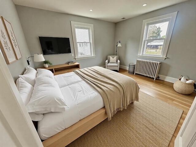 bedroom featuring wood finished floors, visible vents, baseboards, radiator heating unit, and recessed lighting
