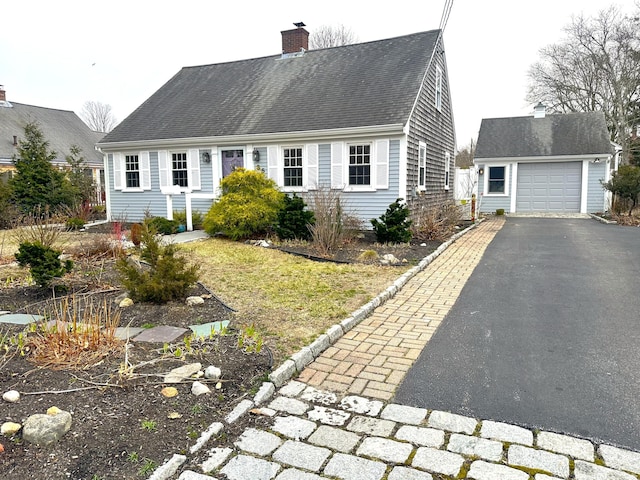 view of front of property featuring a detached garage, roof with shingles, a chimney, an outbuilding, and driveway