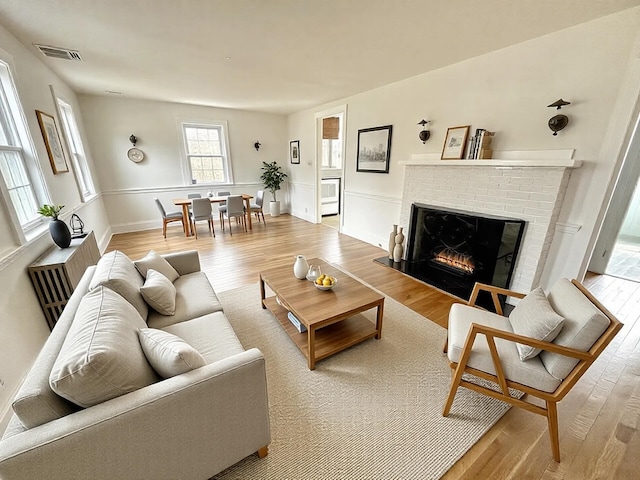 living area with visible vents, a brick fireplace, and wood finished floors