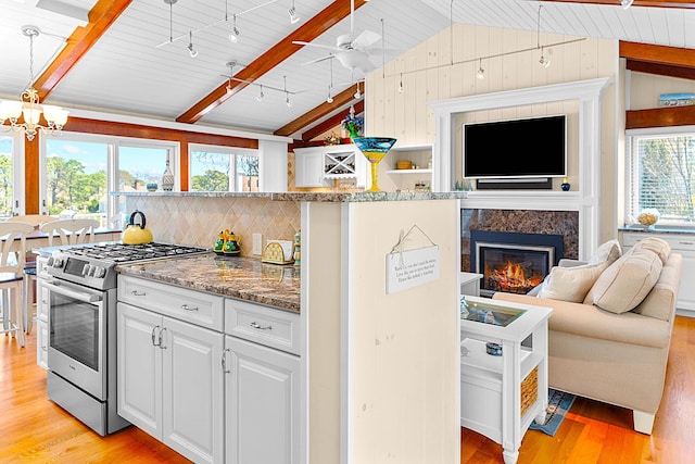 kitchen featuring a fireplace, light wood-type flooring, stainless steel gas range, lofted ceiling with beams, and open floor plan