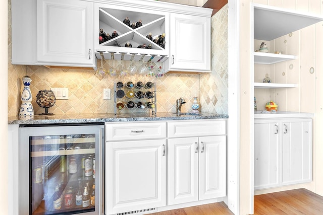 bar with a sink, beverage cooler, light wood-style flooring, decorative backsplash, and a bar