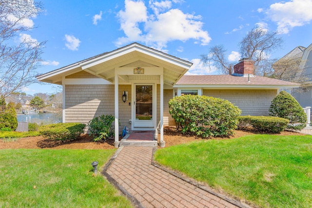 view of front of home featuring roof with shingles, a chimney, and a front yard