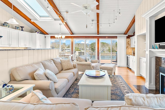 living area featuring track lighting, a fireplace, lofted ceiling with beams, light wood-style flooring, and ceiling fan with notable chandelier