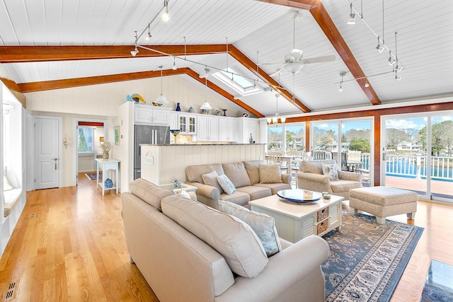 living area featuring track lighting, ceiling fan, lofted ceiling with skylight, and light wood-style flooring