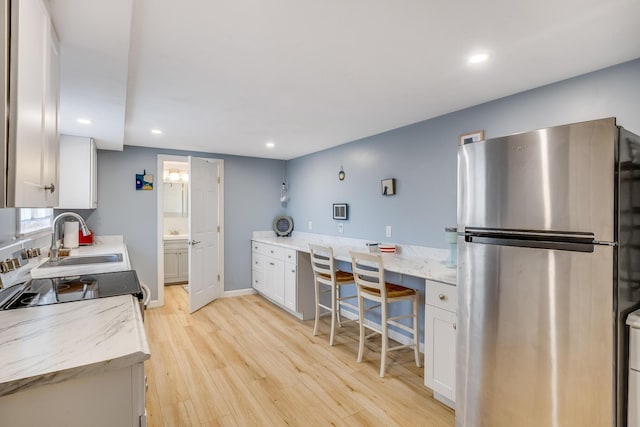 kitchen with light wood finished floors, freestanding refrigerator, electric range, white cabinets, and a sink