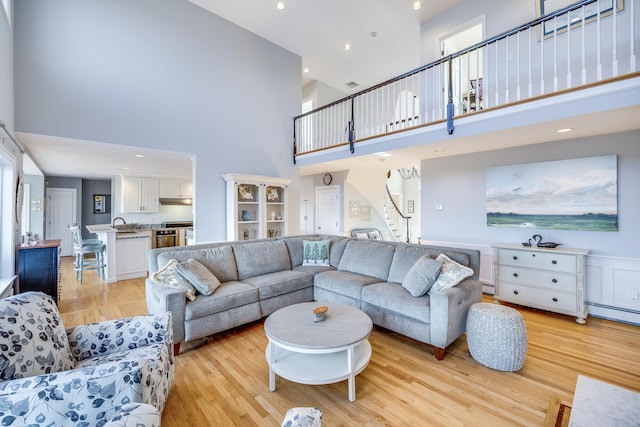 living area with a baseboard radiator, light wood-style floors, a high ceiling, and stairs