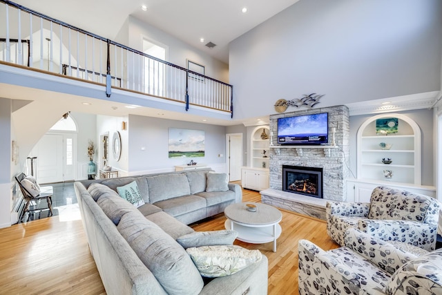 living area featuring a stone fireplace, built in features, visible vents, and wood finished floors