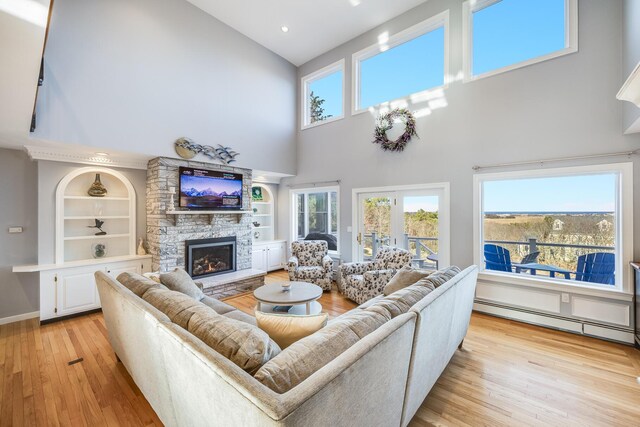 living room featuring built in shelves, baseboards, light wood finished floors, a baseboard radiator, and a fireplace