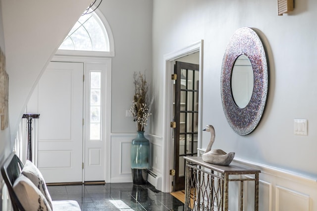 entrance foyer featuring a decorative wall, granite finish floor, and wainscoting