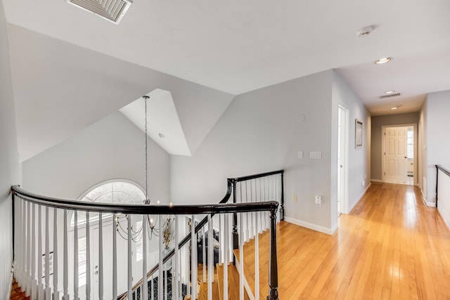 corridor featuring visible vents, baseboards, vaulted ceiling, an upstairs landing, and light wood-style floors