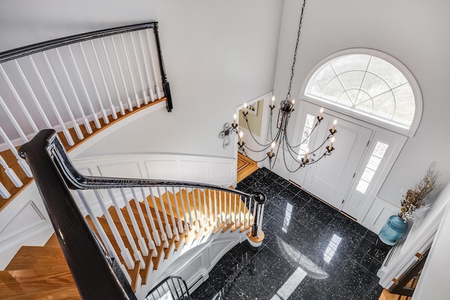 foyer entrance with wainscoting, an inviting chandelier, a towering ceiling, granite finish floor, and a decorative wall