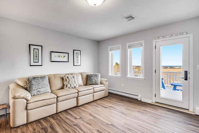 living area featuring a baseboard heating unit, plenty of natural light, visible vents, and wood finished floors