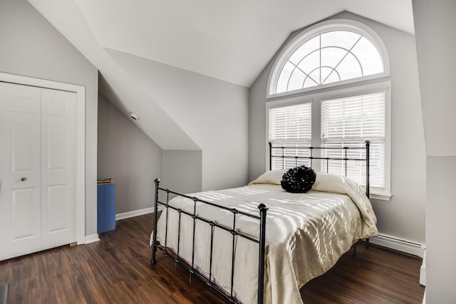 bedroom with baseboards, lofted ceiling, baseboard heating, a closet, and dark wood-style flooring