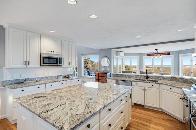 kitchen with a kitchen island, light stone countertops, light wood-style flooring, stainless steel appliances, and a sink