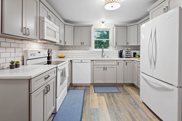 kitchen featuring gray cabinets, sink, decorative backsplash, white appliances, and light hardwood / wood-style flooring