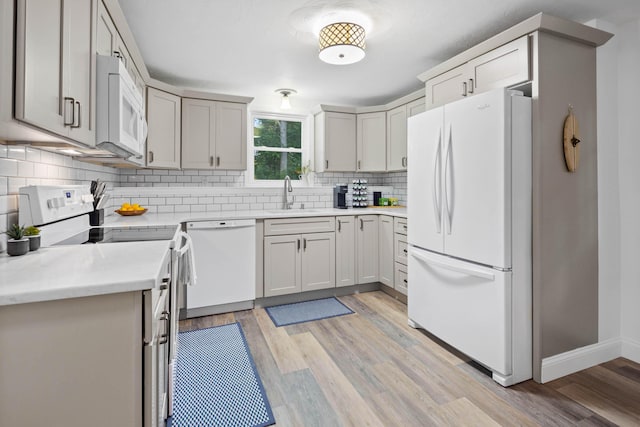 kitchen with sink, backsplash, white appliances, and light hardwood / wood-style floors