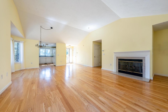 unfurnished living room with baseboards, a fireplace with flush hearth, vaulted ceiling, light wood-style flooring, and a notable chandelier