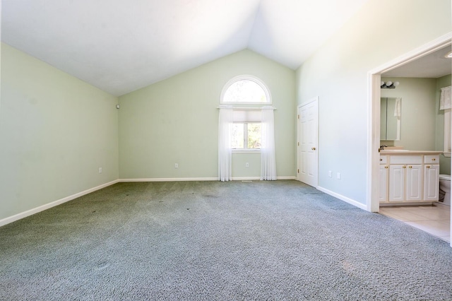 spare room featuring lofted ceiling, light colored carpet, baseboards, and a sink