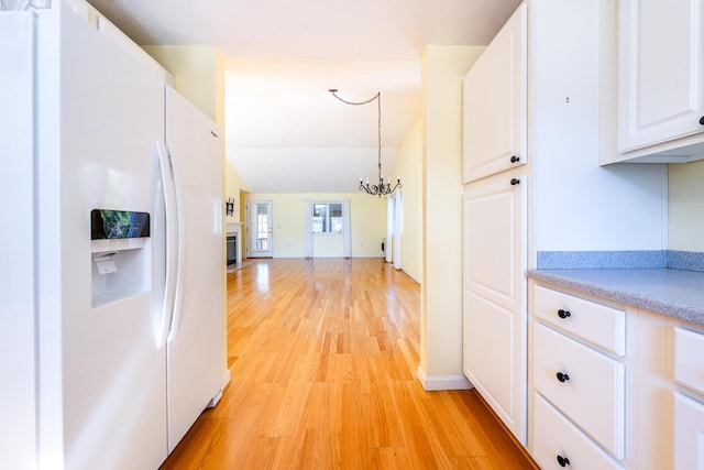 kitchen featuring light wood finished floors, light countertops, white refrigerator with ice dispenser, a notable chandelier, and white cabinets