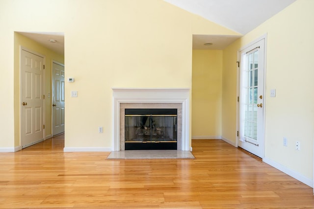 unfurnished living room with a glass covered fireplace, lofted ceiling, light wood-style flooring, and baseboards