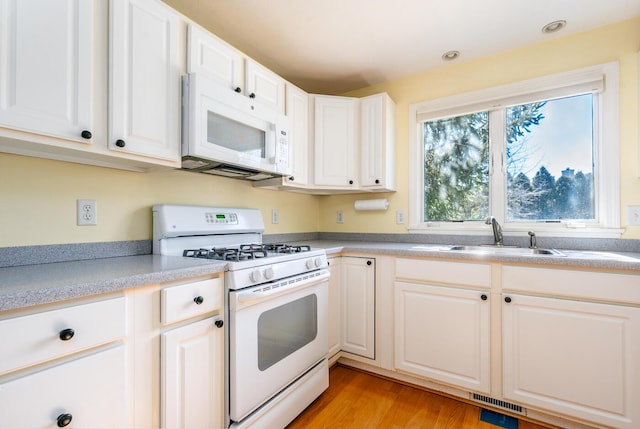 kitchen featuring light wood finished floors, visible vents, light countertops, white appliances, and a sink