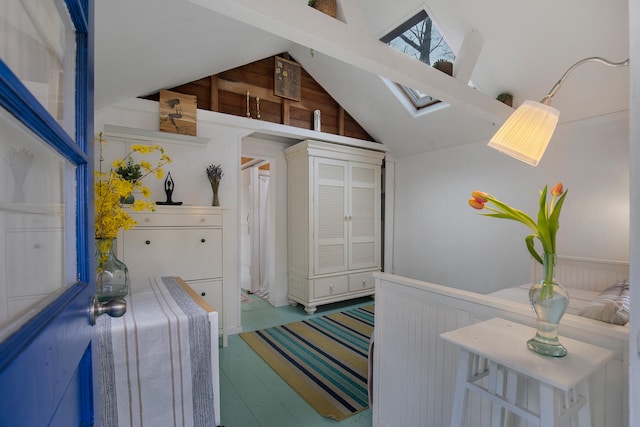 interior space featuring wooden walls, wainscoting, wood finished floors, and lofted ceiling with skylight
