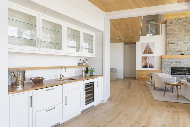 bar featuring butcher block counters, light hardwood / wood-style floors, wood ceiling, sink, and white cabinets