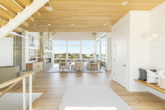 interior space with wood walls, wooden ceiling, light hardwood / wood-style floors, and a stone fireplace