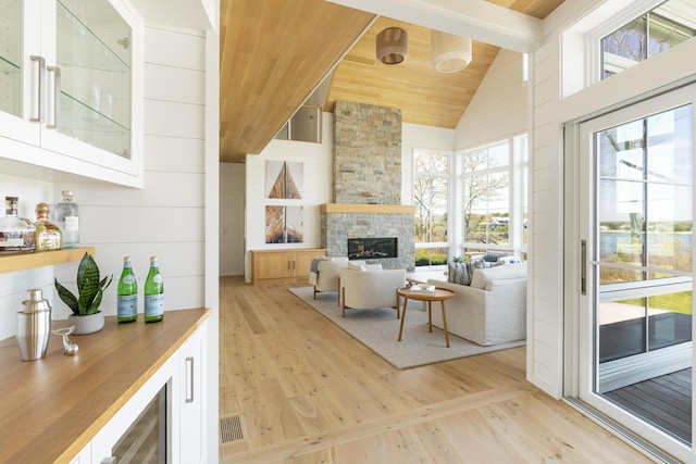 living room featuring a stone fireplace, wood ceiling, high vaulted ceiling, beam ceiling, and light hardwood / wood-style flooring