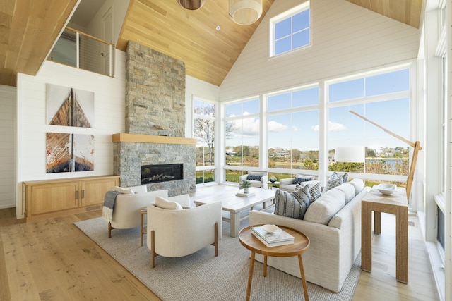 living room with light hardwood / wood-style floors, high vaulted ceiling, a stone fireplace, and wood ceiling