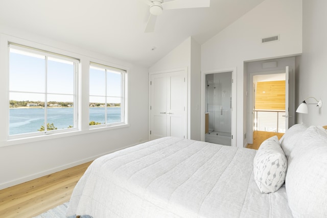 bedroom featuring connected bathroom, hardwood / wood-style flooring, a water view, vaulted ceiling, and ceiling fan