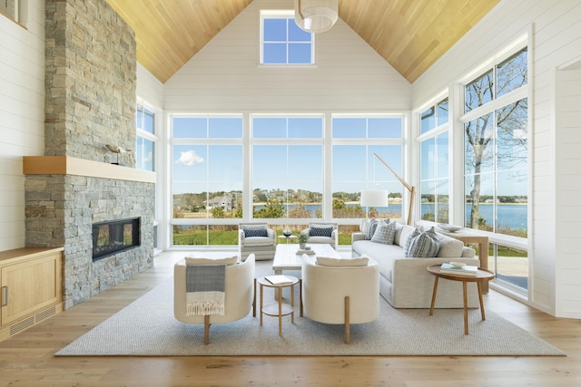 living room featuring a water view, high vaulted ceiling, light hardwood / wood-style flooring, and a fireplace