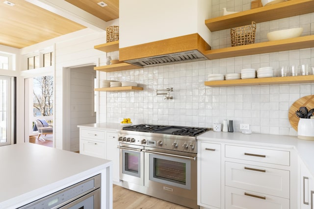 kitchen with light hardwood / wood-style floors, custom range hood, white cabinets, backsplash, and double oven range