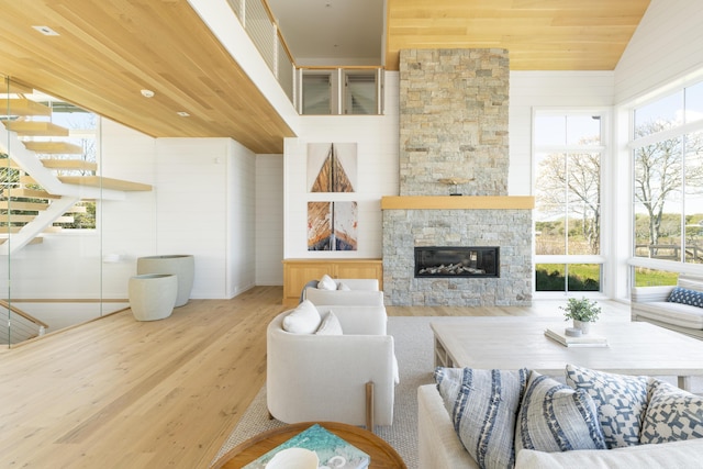 living room featuring wooden ceiling, light hardwood / wood-style floors, a stone fireplace, and plenty of natural light