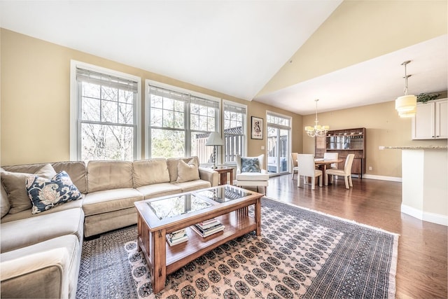 living room featuring a notable chandelier, vaulted ceiling, wood finished floors, and baseboards