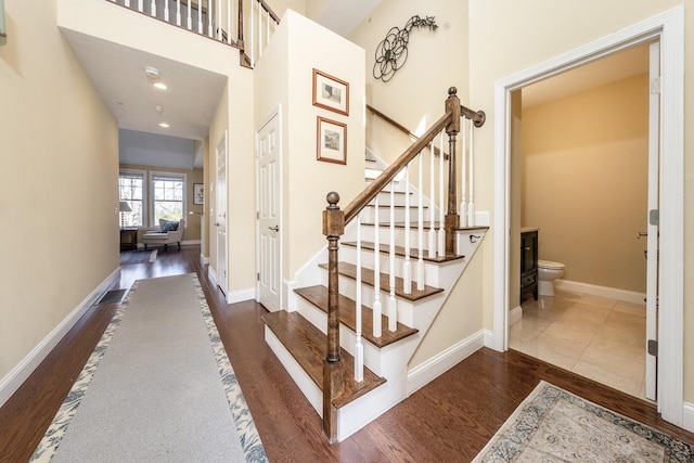stairs featuring wood finished floors, a high ceiling, and baseboards