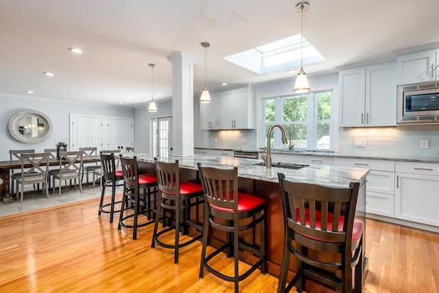 kitchen with stainless steel microwave, decorative light fixtures, light hardwood / wood-style flooring, an island with sink, and light stone counters