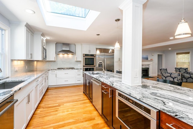 kitchen with hanging light fixtures, wall chimney exhaust hood, built in appliances, and tasteful backsplash