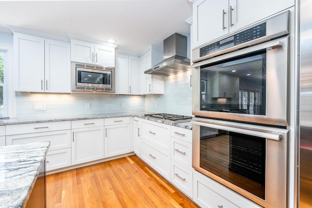 kitchen featuring wall chimney exhaust hood, white cabinetry, stainless steel appliances, tasteful backsplash, and light hardwood / wood-style floors