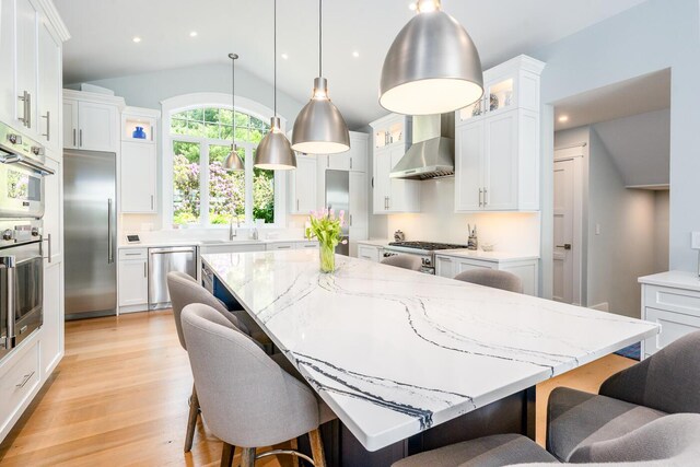 585 Santuit Rd, Cotuit, MA 02635 - kitchen featuring wall chimney exhaust hood, appliances with stainless steel finishes, vaulted ceiling, a large island, and white cabinetry