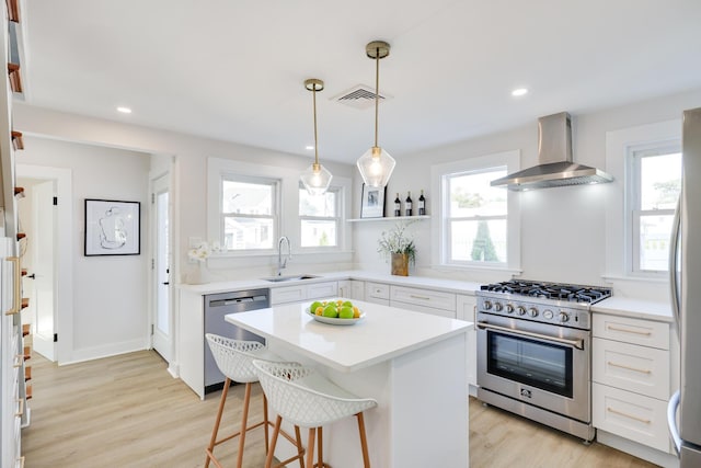 kitchen featuring white cabinets, appliances with stainless steel finishes, a center island, wall chimney range hood, and sink